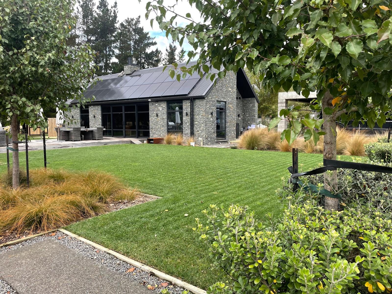 130 Kereru Road — schist and black steel exterior set in lawn and native planting